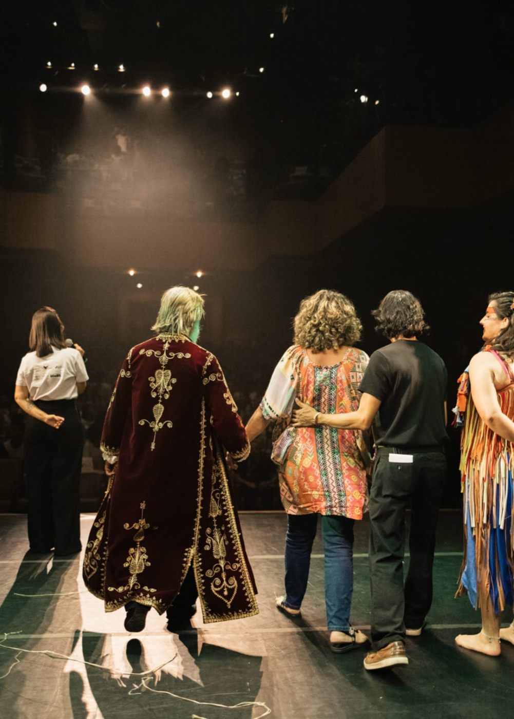 Elenco no palco diante do teatro lotado